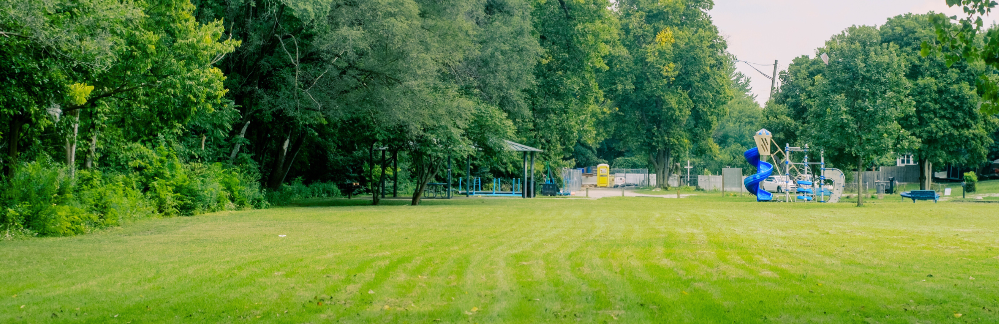 Large open green area in park with playground in the distance