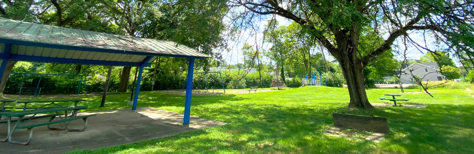 Park with shelter, tree and a playground in the distance