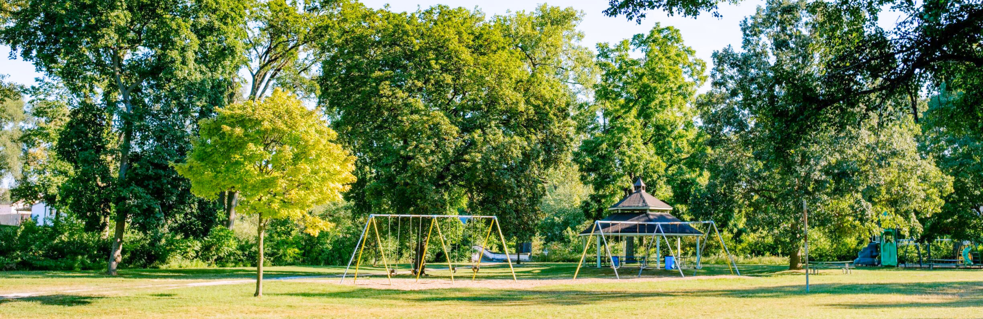 park with open greenspace, a playground in the distance and trees